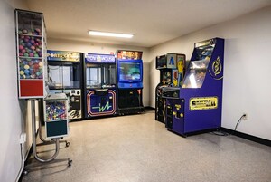 Una habitación con juegos de arcade, una máquina expendedora de bolas de colores y un carrito con dispensador de bebidas.