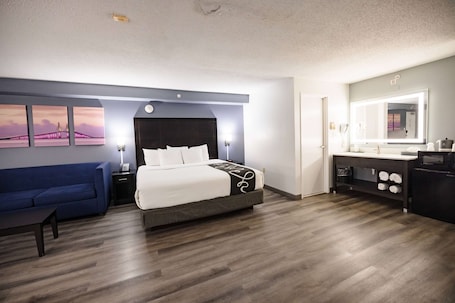 A modern hotel room with a large bed, a blue sofa, a vanity with a mirror, and artwork on the wall.. La Quinta Inn by Wyndham Tampa Near Busch Gardens