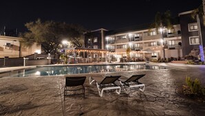 Zona de piscina nocturna con sillones de descanso y una piscina.