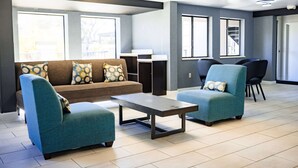 Una sala moderna con un sofá, dos sillones, una mesa de centro y un comedor con sillas y una escalera.