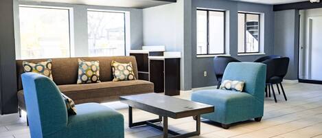 A modern living room with a sofa, two armchairs, a coffee table, and a dining area with chairs and a staircase.