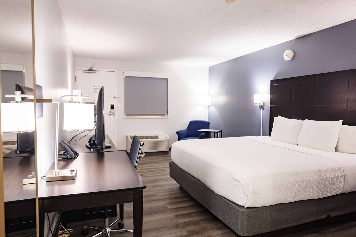 Habitación de hotel con una cama grande, un escritorio con computadora, una silla, una mesita y televisor montado en la pared.