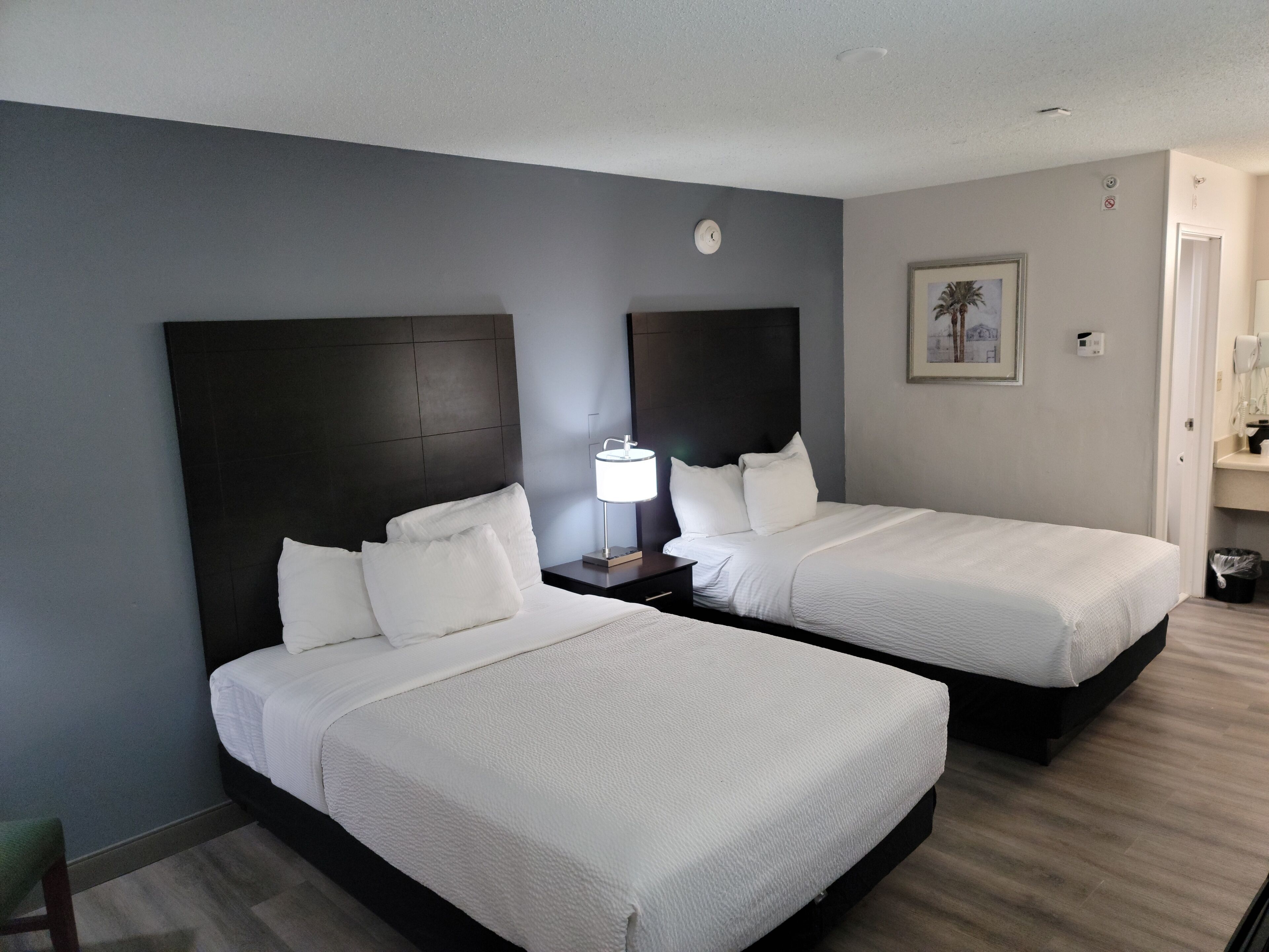 A hotel room with two beds, a nightstand with a lamp, a clock, and a framed picture on the wall.