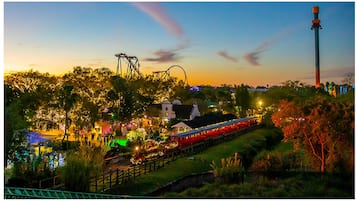 Vista noturna de um parque com montanha-russa, árvores iluminadas e um trem.