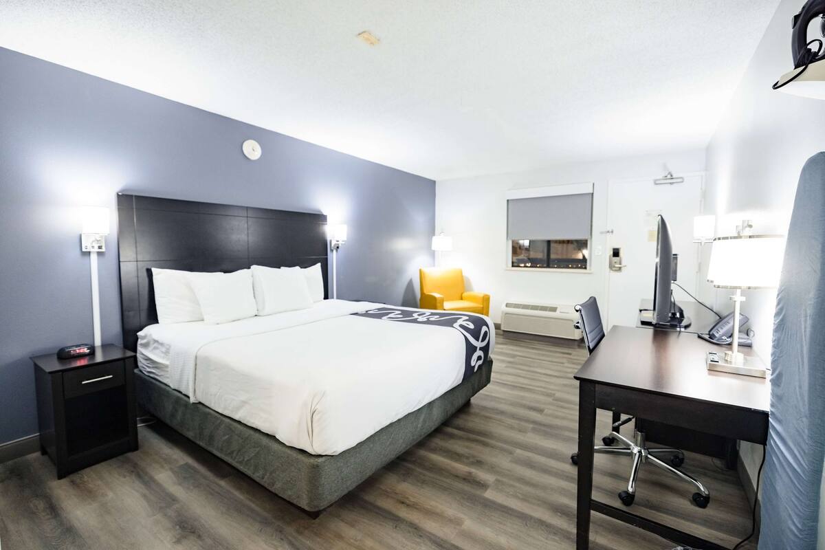 Una habitación de hotel con cama, mesita de noche, escritorio, silla y una pequeña mesa con lámpara.