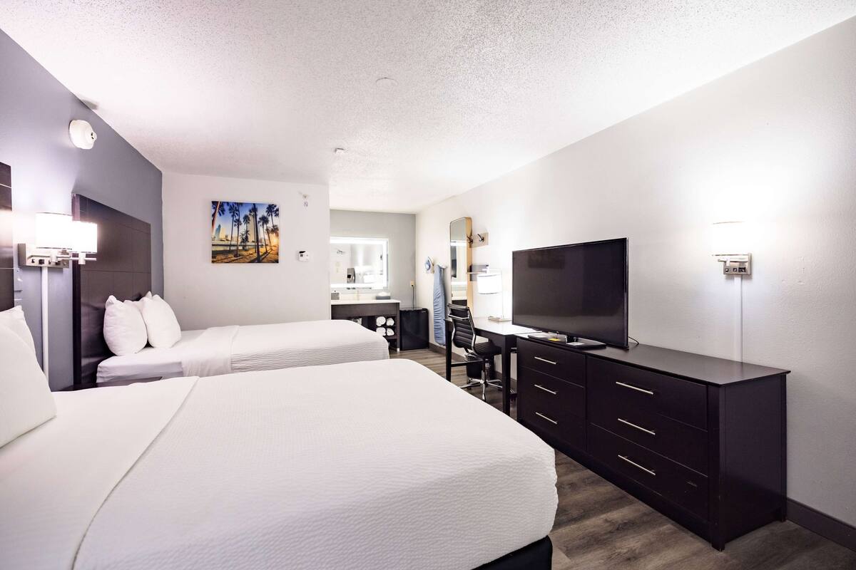 Una habitación de hotel con dos camas, un escritorio, un televisor y un aparador.