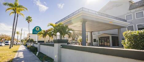 Un hotel con un área exterior techada, palmeras y cielo despejado.