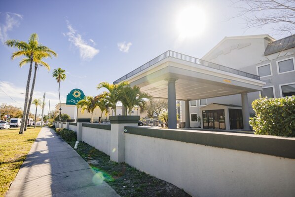 Un hotel con un área exterior techada, palmeras y cielo despejado.