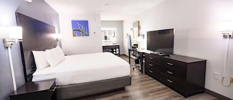 A modern hotel room with a large bed, a desk with a computer, a TV, and a dark wooden dresser.