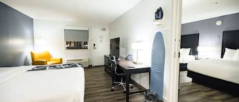 A hotel room with two beds, a desk, a chair, a trash bin, and a door leading to another room.