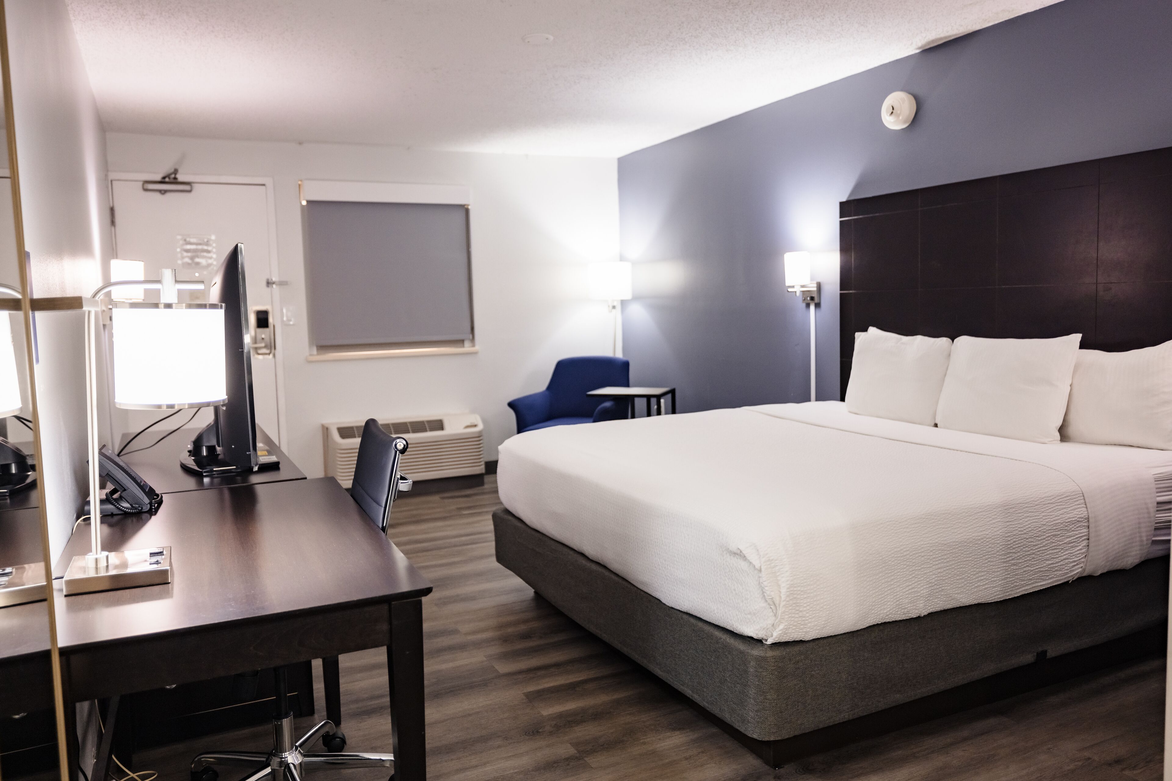 A hotel room with a large bed, a desk with a computer, a chair, and a lamp.