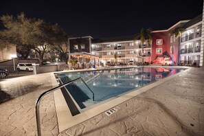 Une piscine dont la profondeur maximale est de 3 pieds, entourée d’un bâtiment doté de balcons et d’un espace couvert aménagé avec des chaises longues.