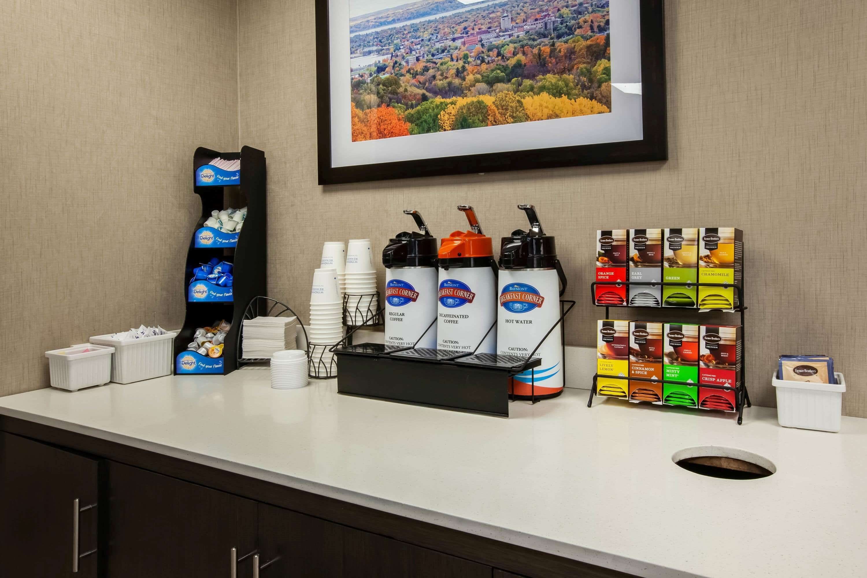 A coffee station with disposable cups, a coffee dispenser, and a variety of coffee flavors.