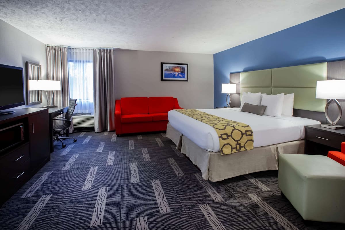 Une chambre d’hôtel avec un lit, un canapé rouge, un bureau avec une télévision et une lampe.