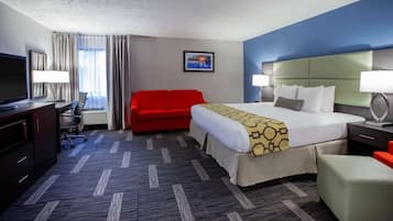 A hotel room with a bed, a red sofa, a desk with a TV, and a lamp.