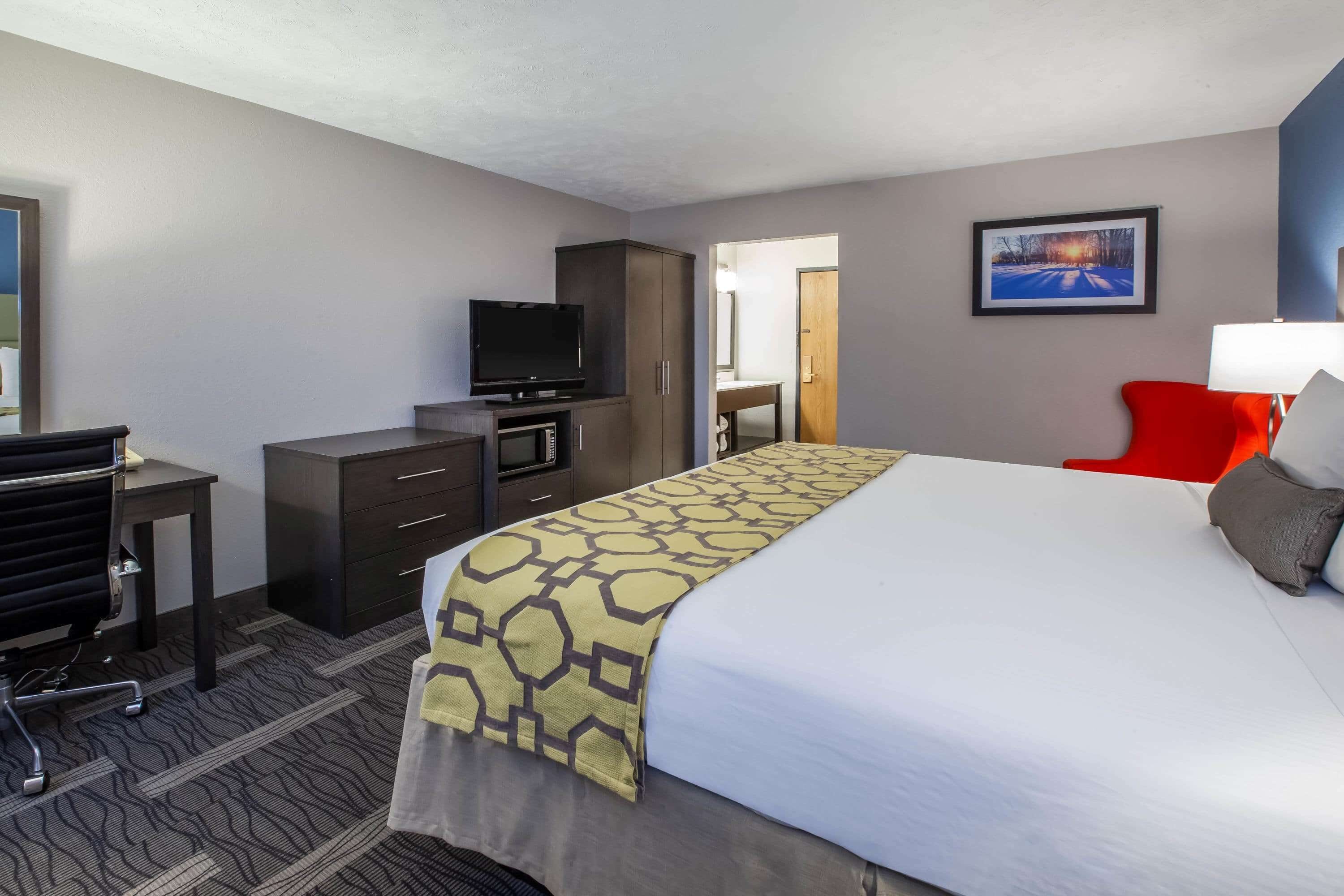 A hotel room with a bed, a desk with a chair, a television, a wardrobe, and a painting on the wall.