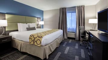 Habitación de hotel con una cama grande, un escritorio con computadora, televisor y ventana con cortinas.