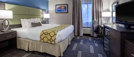 A hotel room with a large bed, a desk with a flat-screen TV, a chair, and a window with curtains.