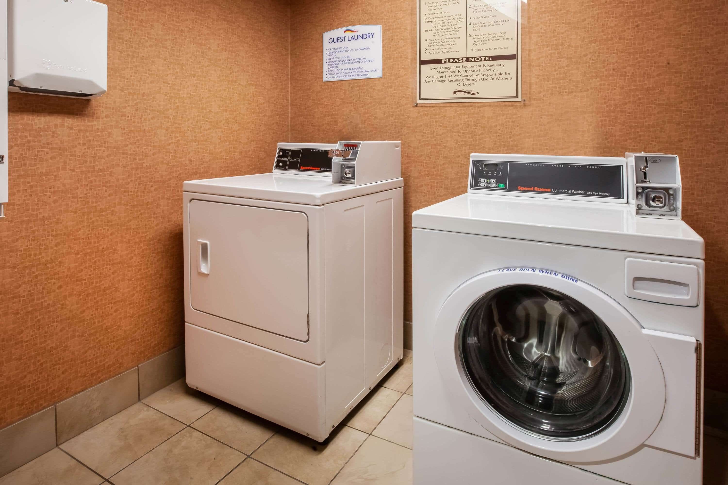 A laundry room with a front-loading washer and dryer, a sign indicating guest laundry services, and a wall-mounted air conditioning unit.