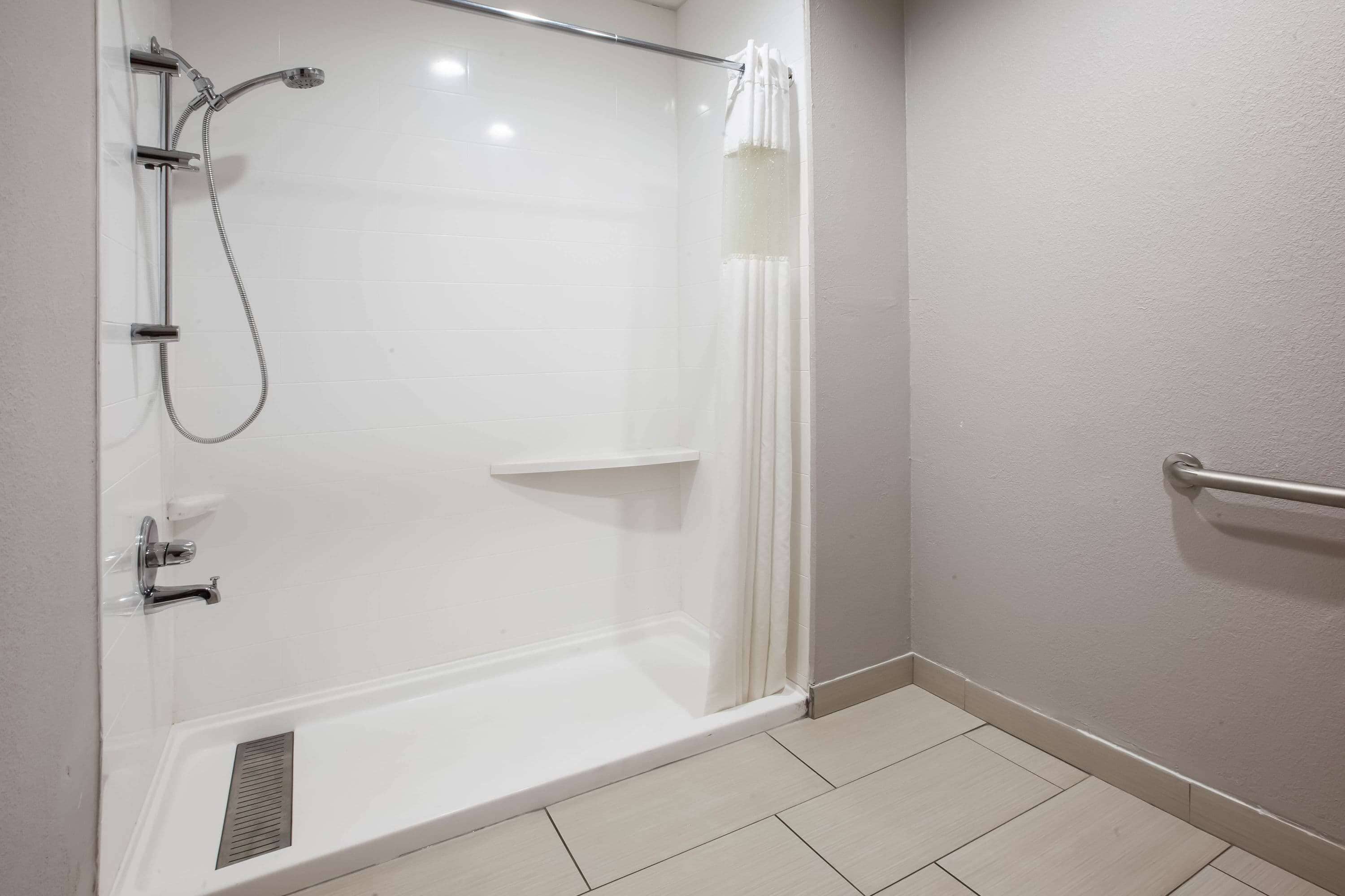 Ein modernes Badezimmer mit einer gläsernen Duschkabine, weißen Fliesen und einer Haltestange.