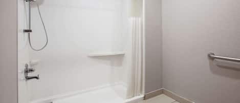 A modern bathroom with a glass-enclosed shower, a white tiled floor, and a metal grab bar.