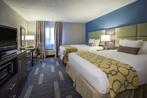 A hotel room with two beds, a television, a desk with a lamp, and a view of the outdoors.