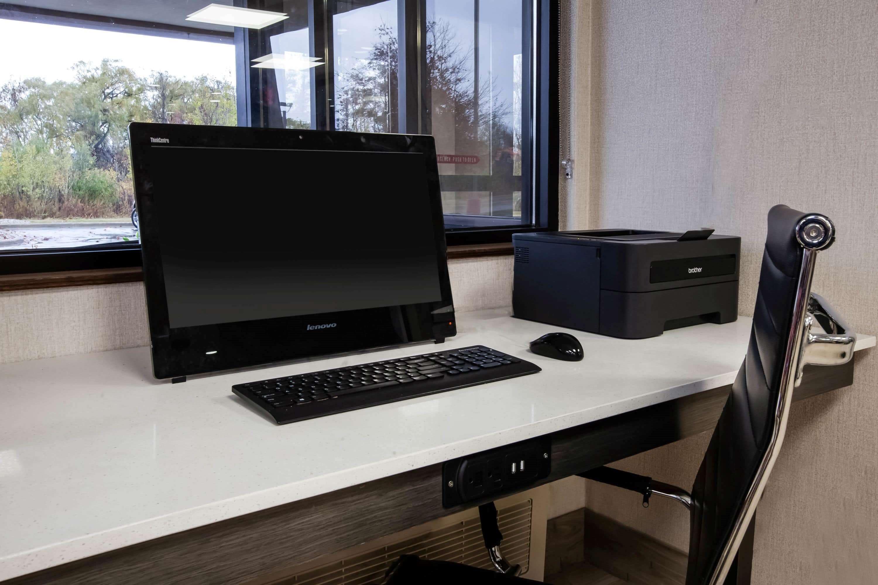 A desk with a Lenovo laptop, a Brother printer, a mouse, and a chair.