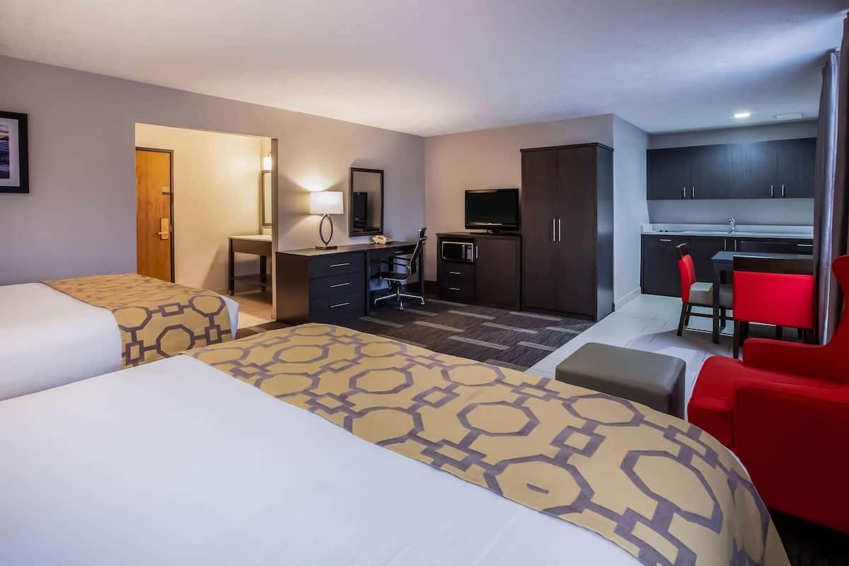 Une chambre d’hôtel avec deux lits, un bureau, une télévision, une kitchenette et une chaise rouge.