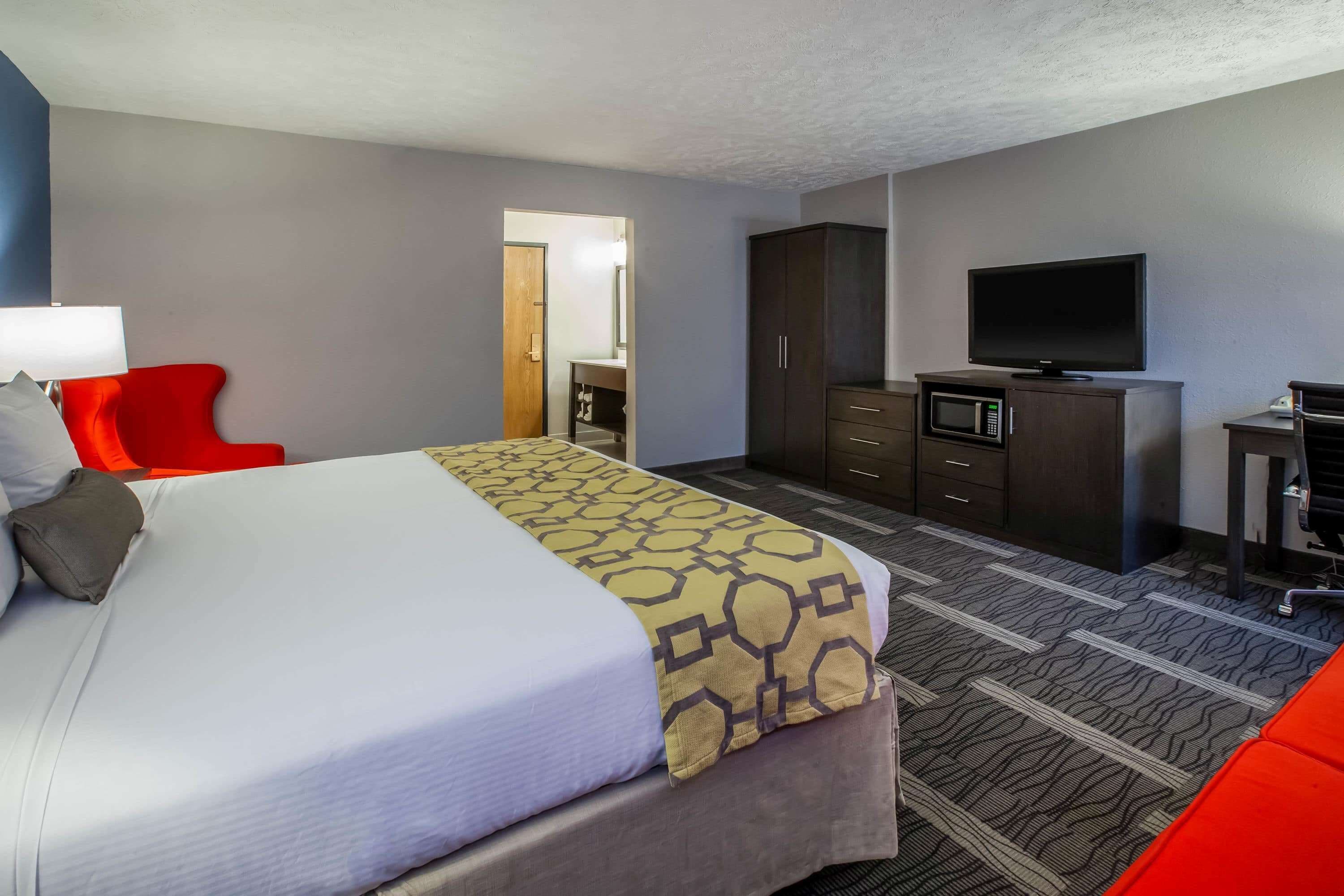 Une chambre d’hôtel avec un grand lit, un fauteuil rouge, une télévision, une armoire et un four à micro-ondes.