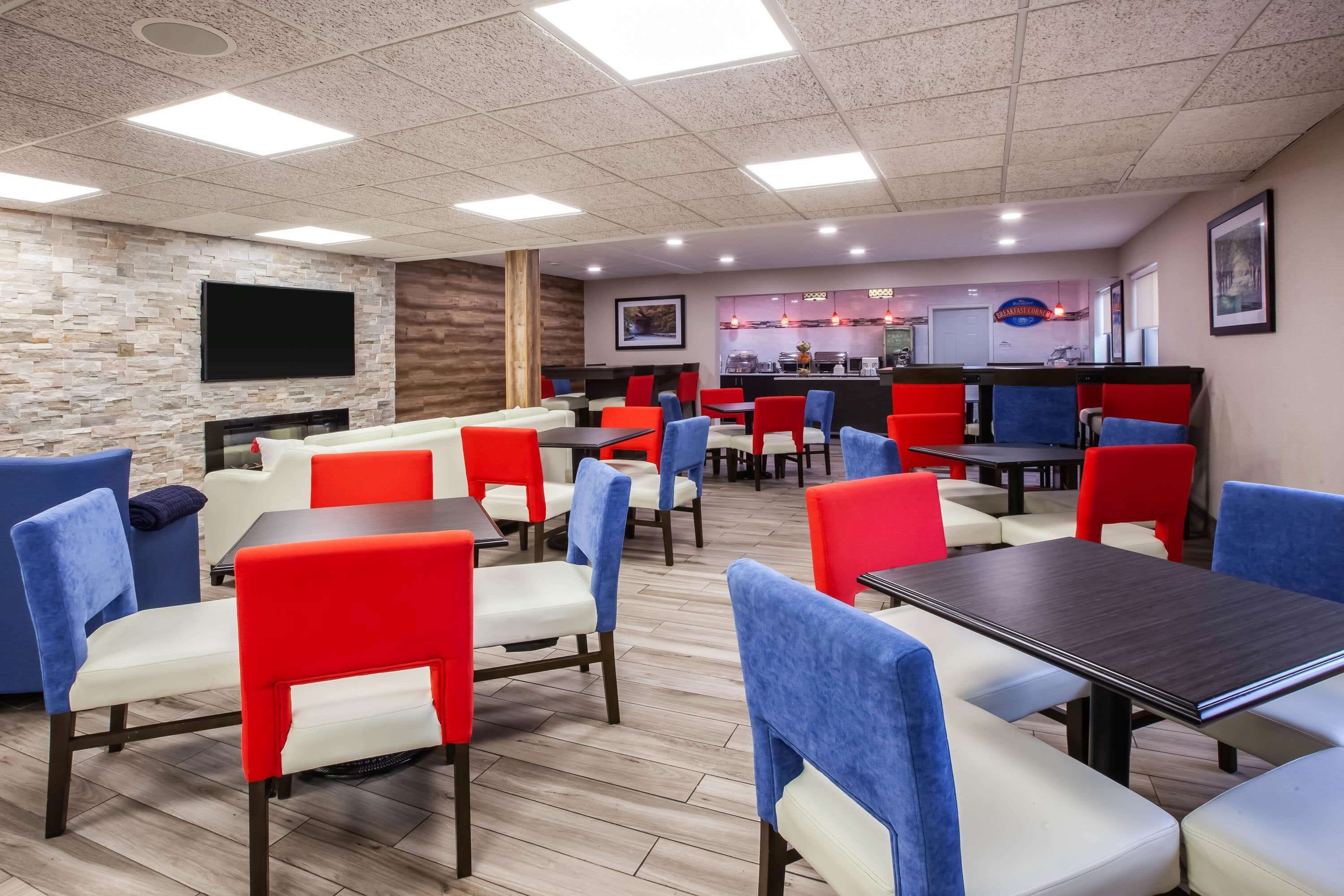 A restaurant with multiple tables and chairs, a kitchen area, and a flat-screen TV mounted on the wall.