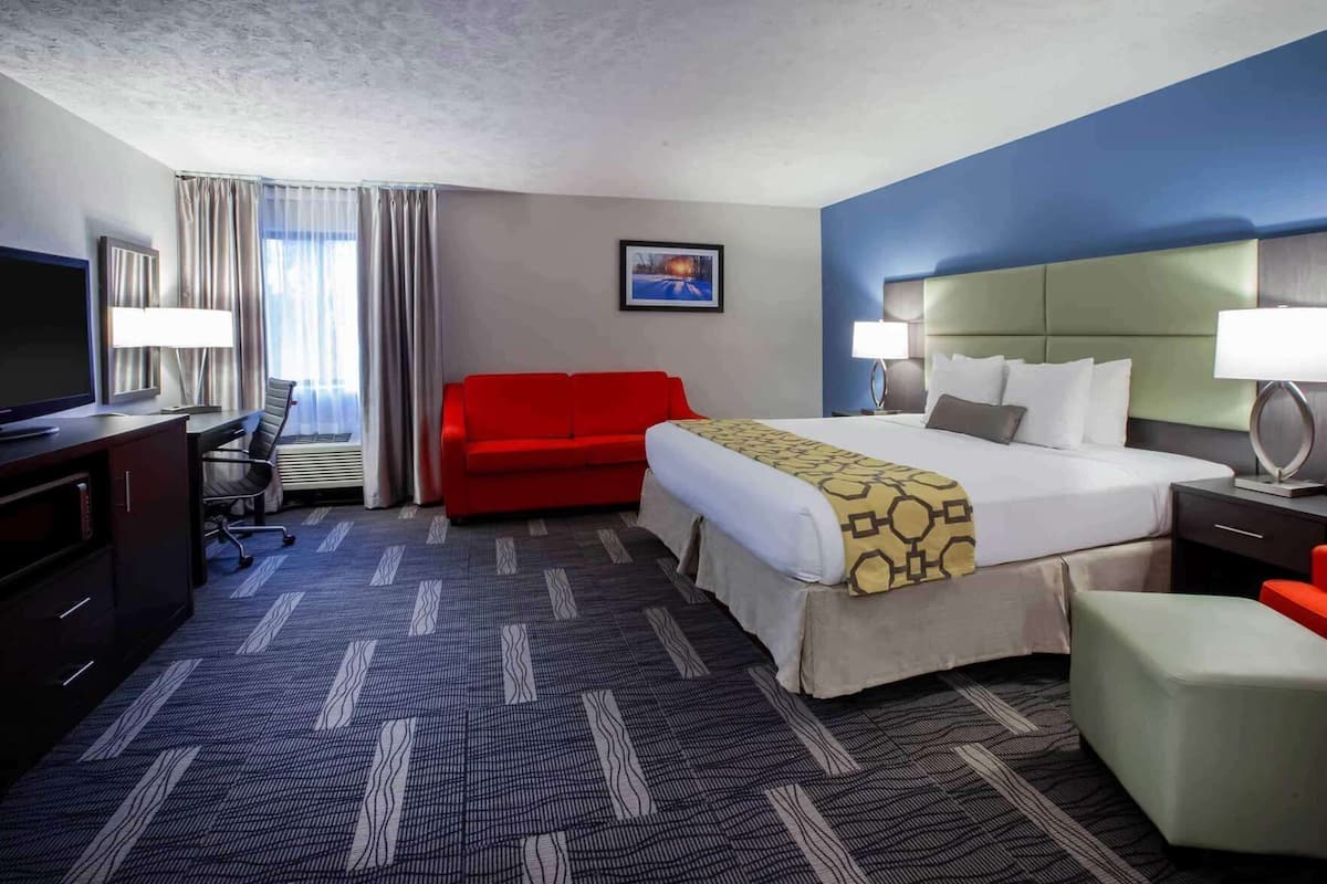 Une chambre d’hôtel avec un lit, un bureau avec un ordinateur, un canapé rouge et un téléviseur.