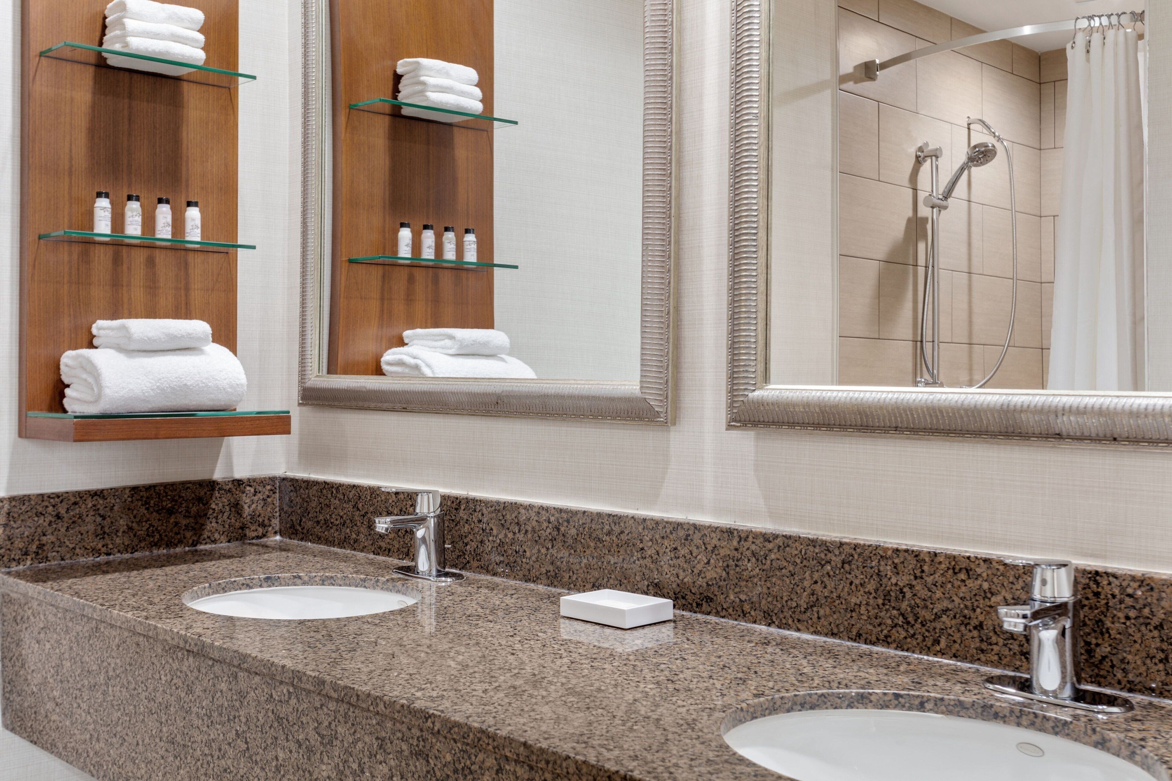 A modern bathroom with two sinks, a large mirror, and shelves with towels and toiletries.