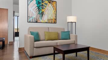 Uma sala de estar moderna com um sofá bege, duas almofadas, uma mesa de centro de madeira, um abajur e um grande quadro abstrato na parede.