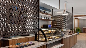 A modern cafe with a wooden counter, a glass display case with pastries, and a decorative lattice partition. - Delta Hotels by Marriott Bristol (Bristol)