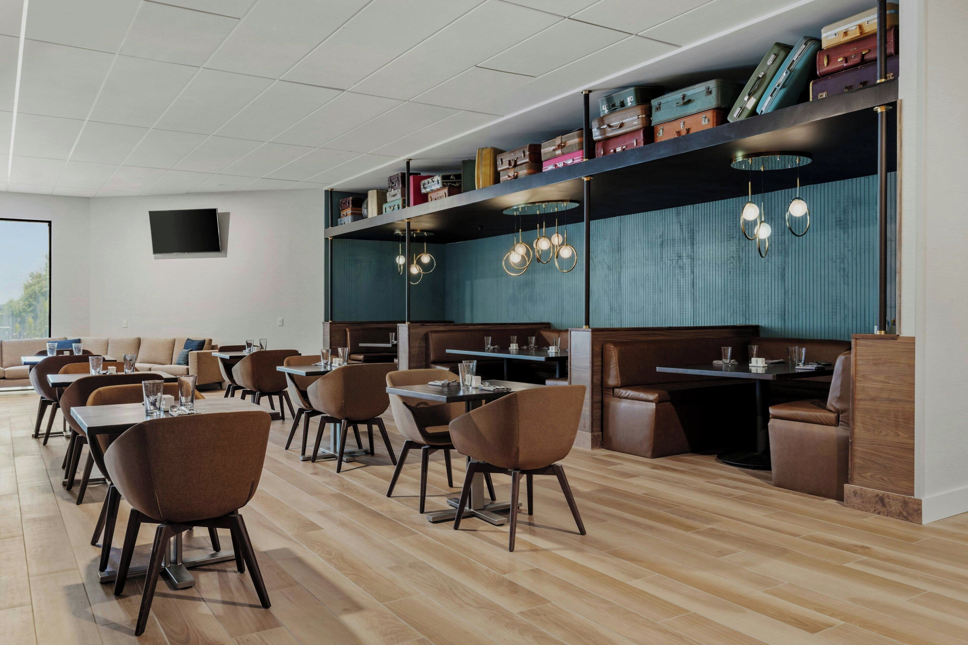 Un restaurant moderne avec un plancher en bois, des chaises recouvertes d’un tissu marron et diverses valises disposées sur des étagères.