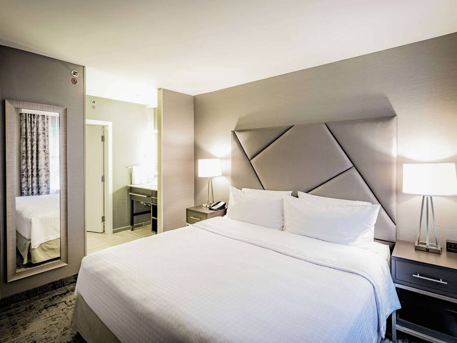 Une chambre d’hôtel avec un grand lit, une table de chevet avec une lampe, un miroir et une porte donnant sur une salle de bain.