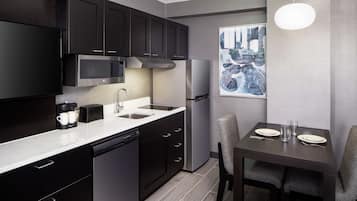 Una cocina moderna con armarios oscuros, microondas, refrigerador, lavavajillas y una mesa de comedor con sillas.