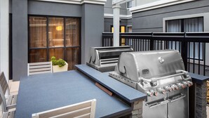 Une terrasse extérieure équipée d’un barbecue, d’un espace salon et offrant une vue sur l’intérieur du bâtiment.