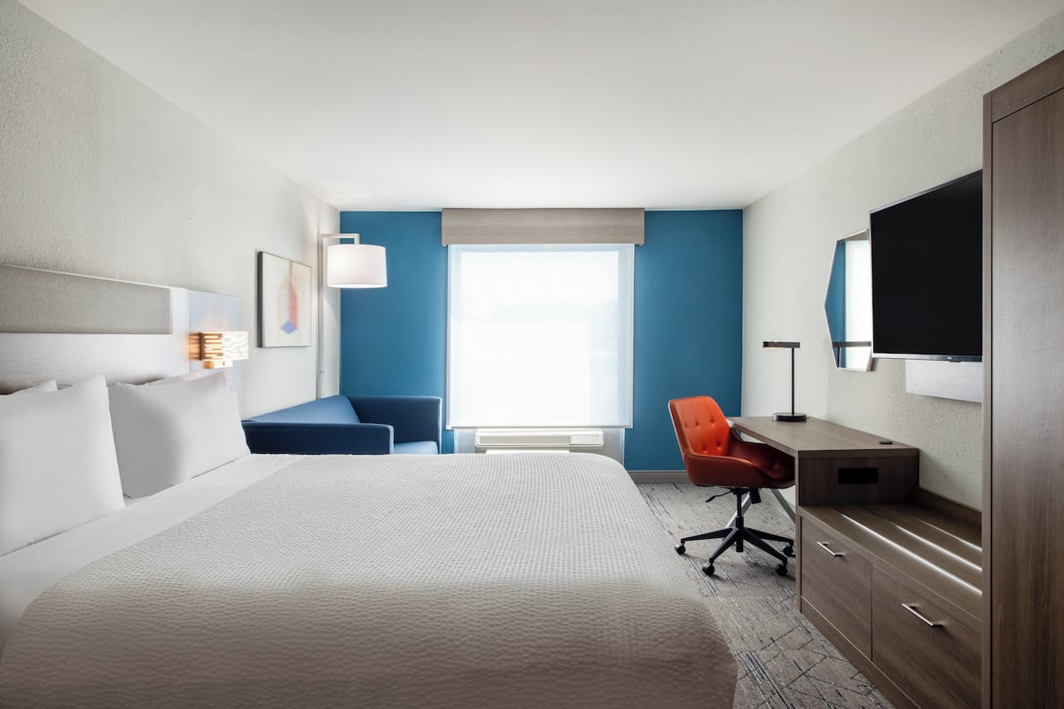 Habitación de hotel con una cama grande, un escritorio con silla, televisión y ventana con persianas.