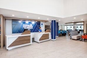 A modern reception area with two counters, a seating area with tables and chairs, and a large window providing natural light. - Holiday Inn Express Hotel & Suites Wilson - Hayes Place by IHG (Wilson)