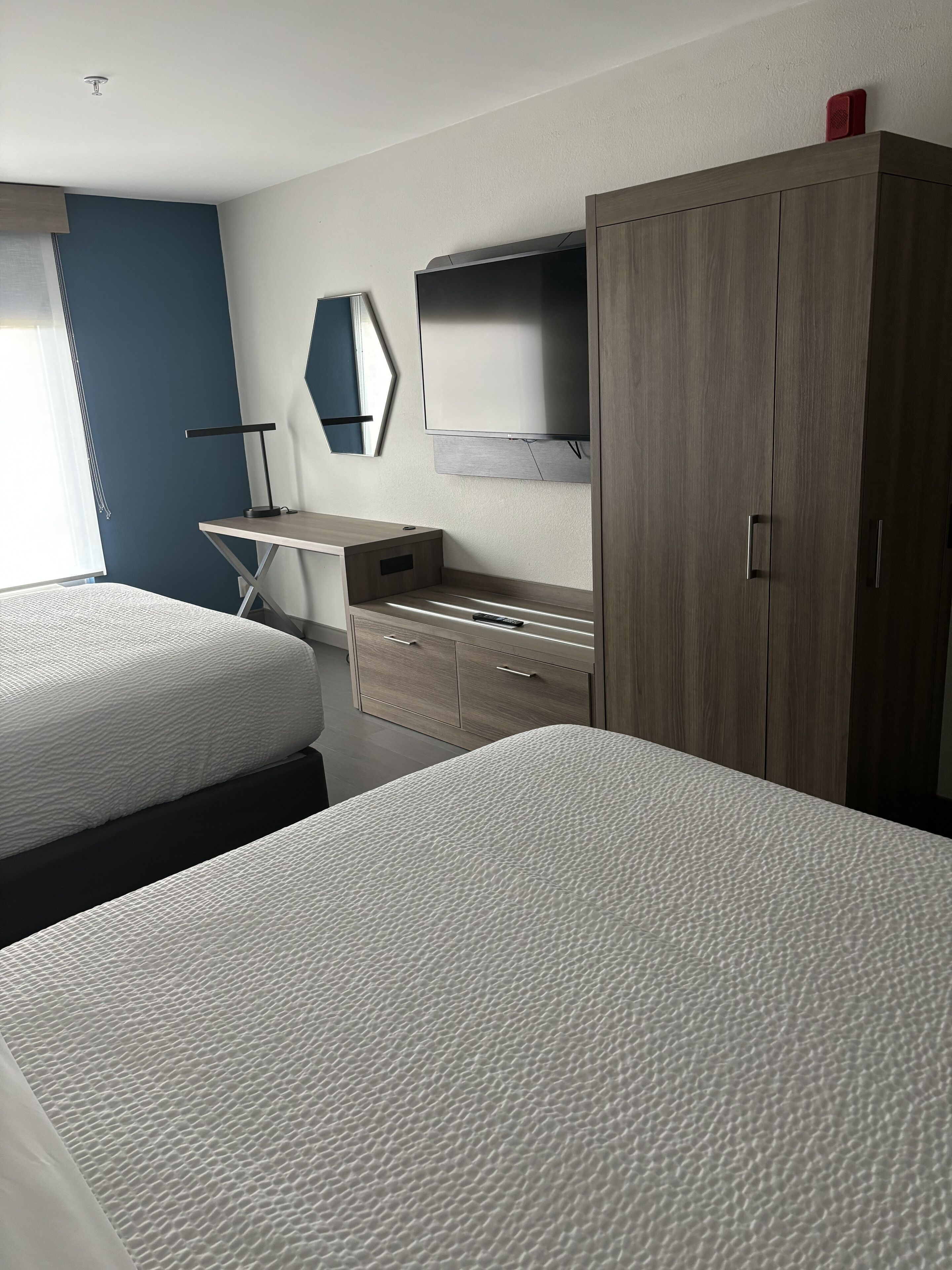 A hotel room with two beds, a desk, a wardrobe, and a TV.