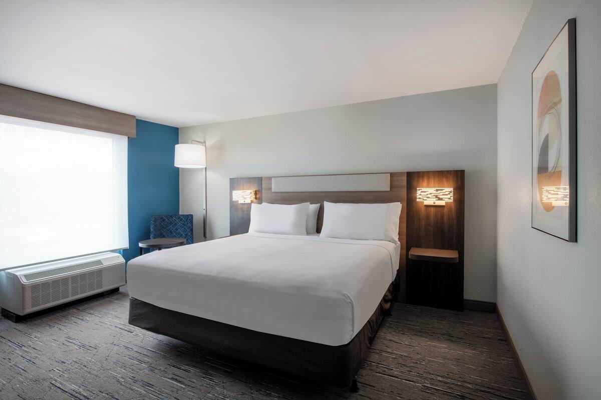 Habitación de hotel con una cama grande, una mesita de noche, una lámpara y una obra de arte colgada en la pared.