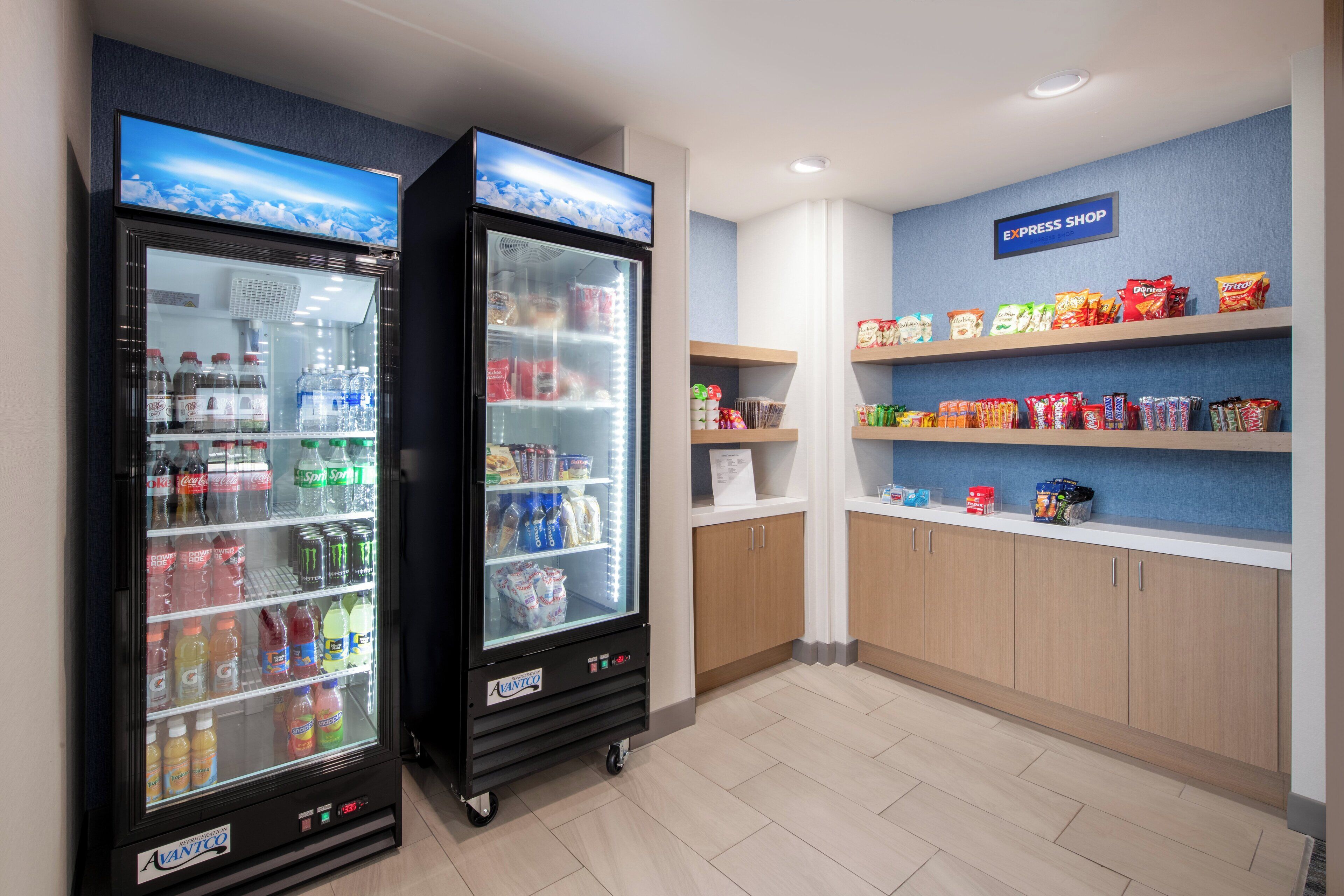 Deux distributeurs automatiques de boissons proposant une variété de breuvages, un présentoir à collations et un panneau indiquant l’emplacement d’une boutique proposant des produits à emporter.