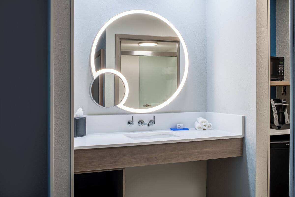Et moderne badeværelse med et rundt spejl, en vask og et toilet.