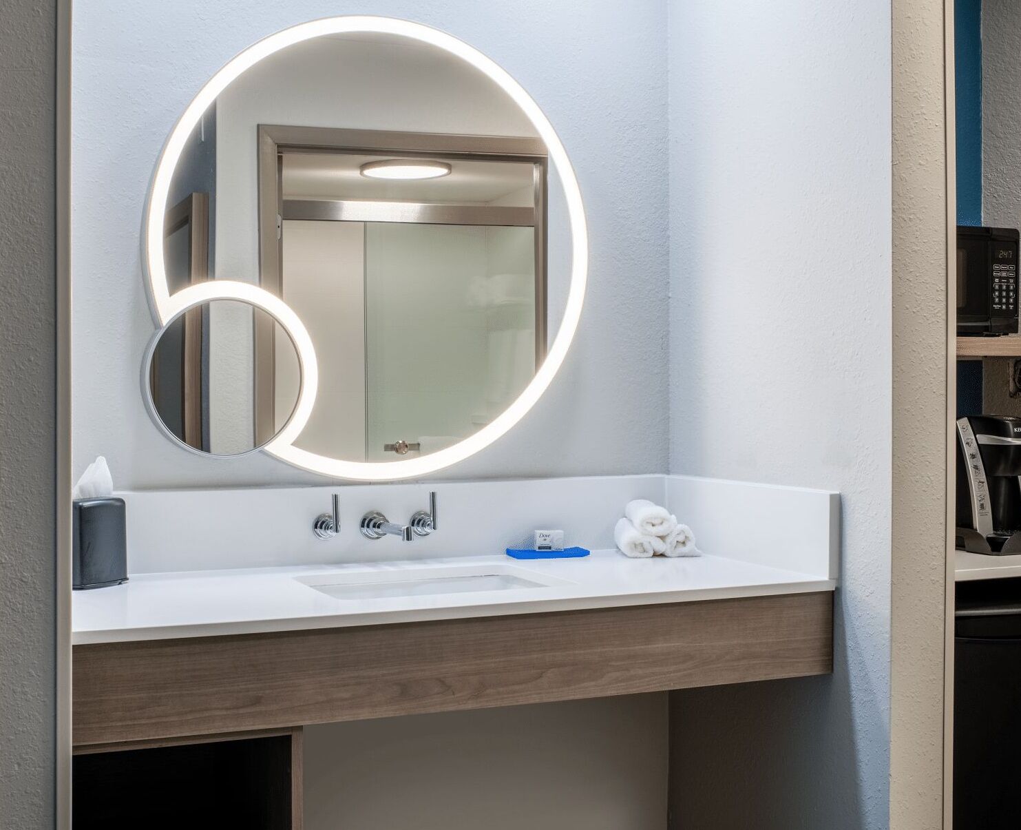 A modern bathroom with a round mirror, a white sink, and a towel rack.