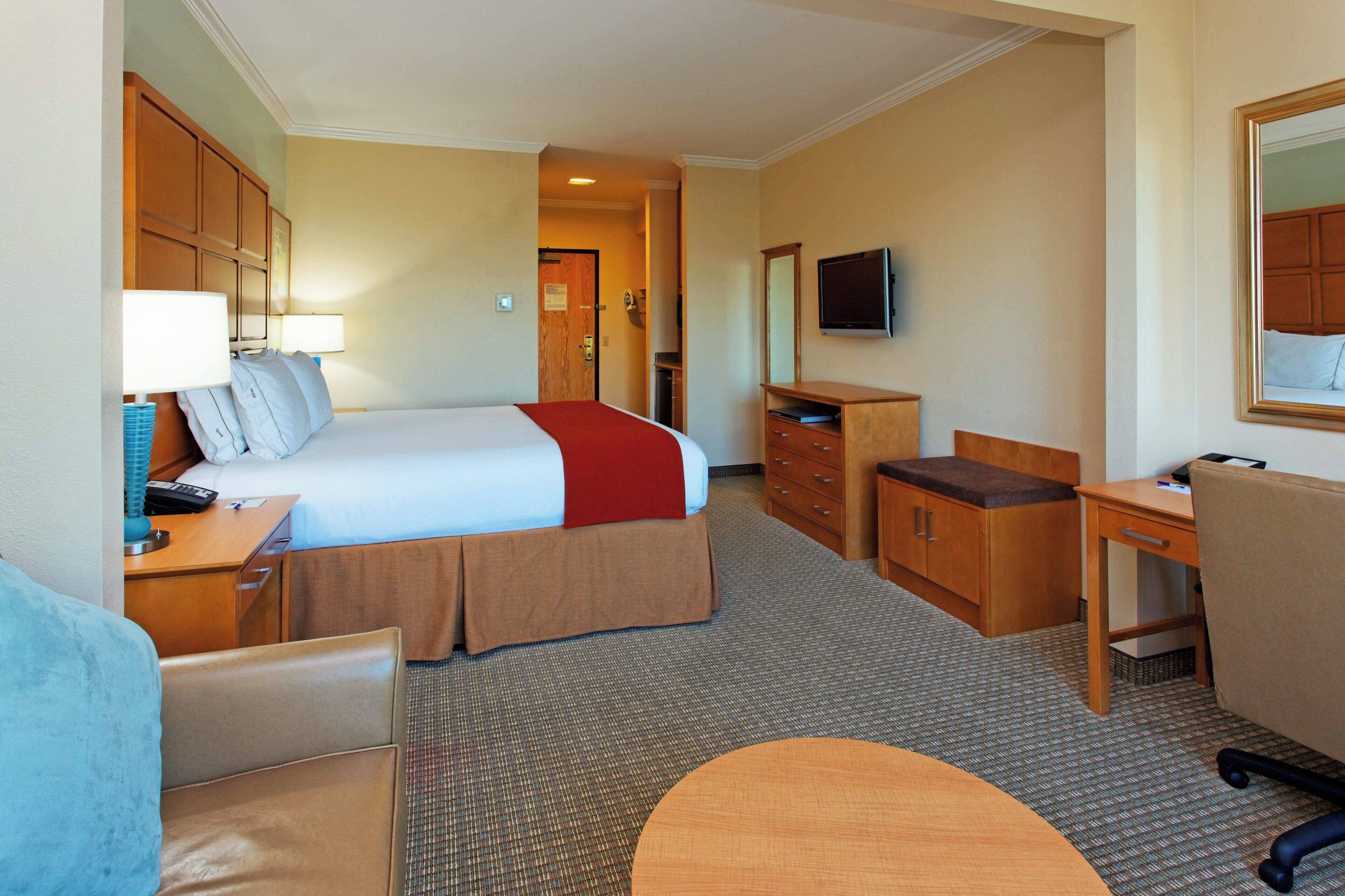 A hotel room with a bed, a desk, a chair, a dresser, a television, and a mirror.