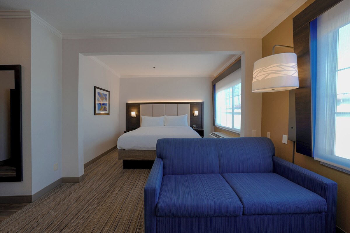 A hotel room with a bed, a blue sofa, a wall-mounted lamp, and a framed picture on the wall.