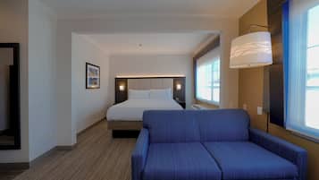 Quarto de hotel com cama, sofá azul, luminária na parede e quadro emoldurado.