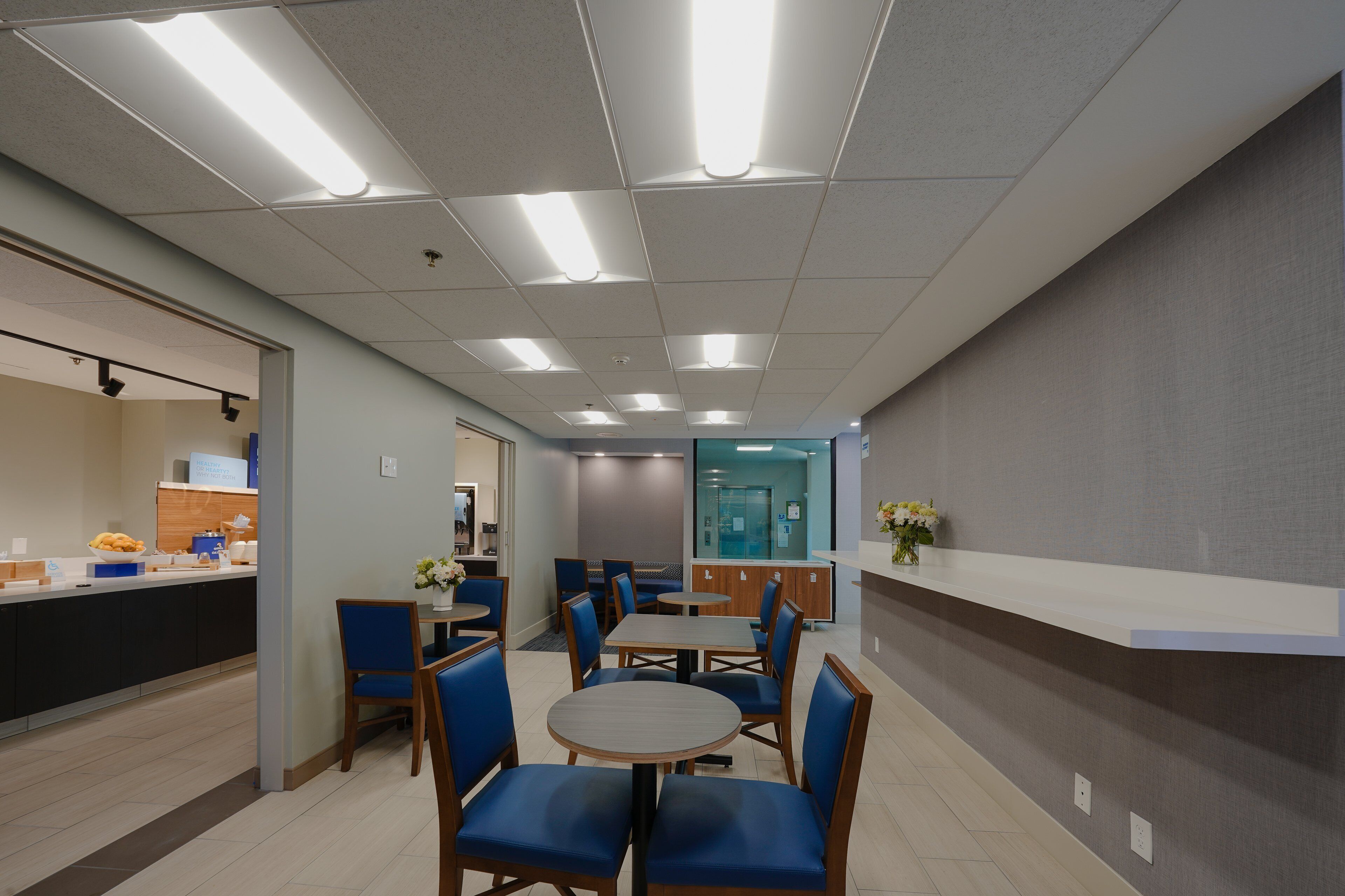 A modern dining area with round tables and blue chairs, a counter with food items, and a reception desk.