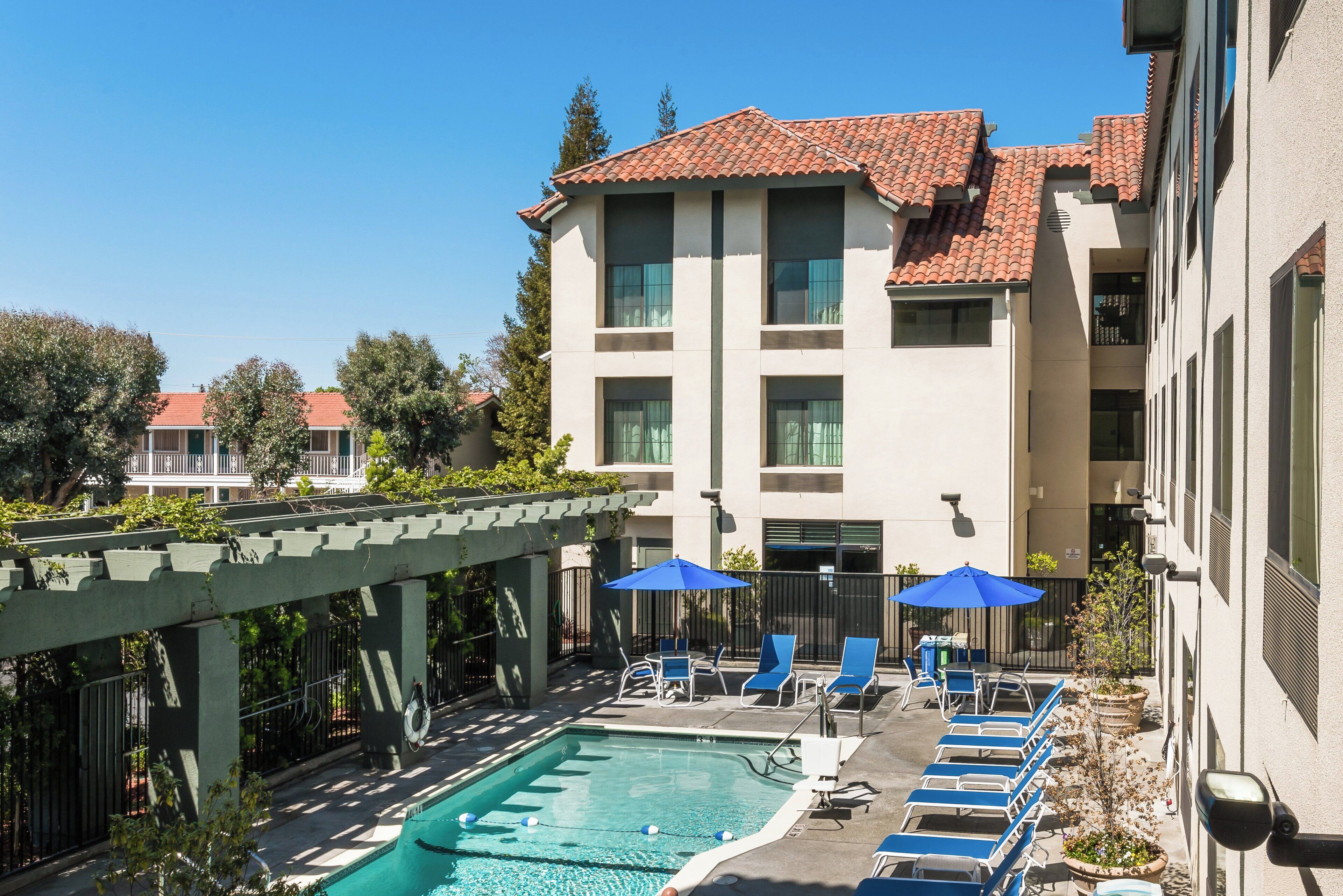 A hotel with a swimming pool, lounge chairs, and umbrellas.